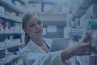 Female pharmacist is searching medicines on shelves with blue filter